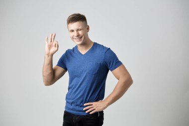 Mavi t-shirt giymiş adam memnun hissediyor ve gösterileri Tamam parmaklarıyla işaret. Beyaz arka plan üzerinde atış stüdyo
