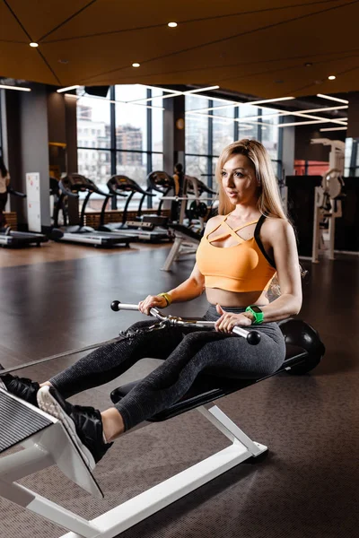 운동복을 입고 긴 금발 머리를 가진 아름 다운 운동 소녀는 현대적인 체육관에서 벤치에 장비와 스포츠 연습을 하 — 스톡 사진