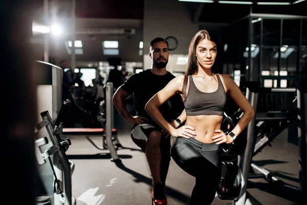 Menina atlética de cabelos escuros vestida com roupas esportivas pretas e treinador de fitness estão fazendo aquecimento no ginásio — Fotografia de Stock