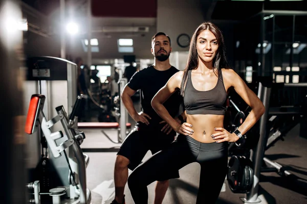 İnce esmer kız siyah spor kıyafetlerini giymiş ve spor hocası yapıyor sıcak spor salonunda