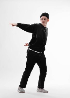 Genç dansçı siyah kot, tişört, şapka ve gri spor ayakkabı giymiş freestyle beyaz arka plan üzerinde stüdyoda dans ediyor