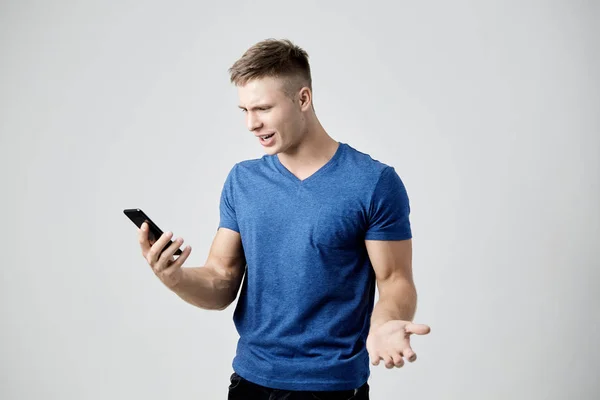 O cara vestido de camiseta azul parece surpreso com seu telefone celular — Fotografia de Stock