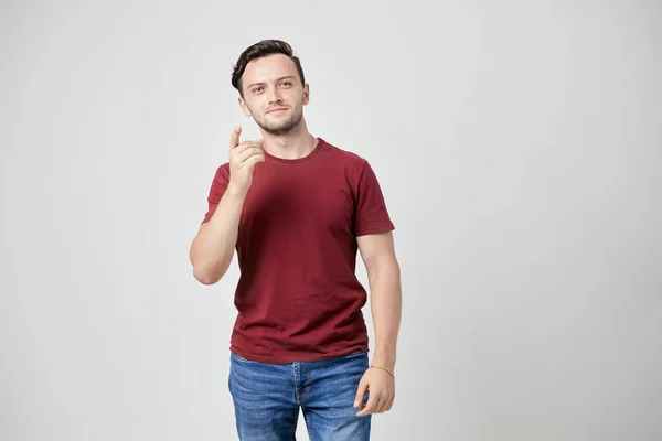 Задумчивый мужчина в бордовой футболке показывает пальцем вверх — стоковое фото