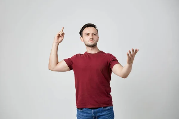 Задумчивый мужчина в бордовой футболке показывает пальцем вверх — стоковое фото