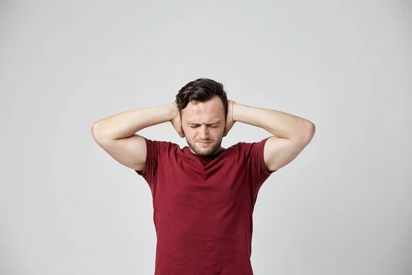 Раздражённый мужчина в бордовой футболке закрыл уши руками — стоковое фото