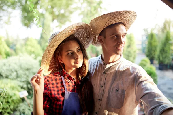 Gardeners cara romântico e menina em um chapéu de palha estão de pé no maravilhoso jardim em um dia ensolarado . — Fotografia de Stock