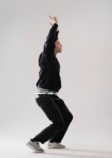 Cara vestida com jeans pretos, capuz e tênis cinza está dançando segurando a mão no estúdio no fundo branco no estúdio — Fotografia de Stock