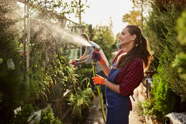 Niña jardinero rocía plantas de agua en el hermoso vivero-jardín en un día soleado. Trabajando en el jardín — Foto de Stock