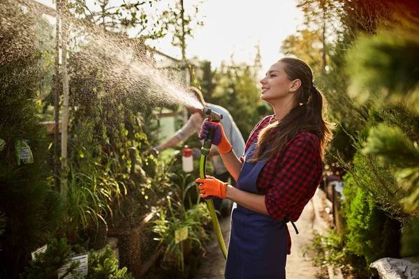 Niña jardinero rocía plantas de agua en el hermoso vivero-jardín en un día soleado. Trabajando en el jardín — Foto de Stock