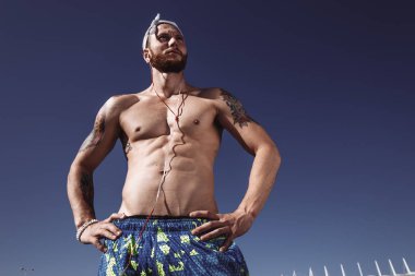 Açık havada egzersiz zeminde eğitimden sonra rahatlatıcı. Yakışıklı gömleksiz sporcu uzakta müzik kentsel poz dinleme earphones ile parlak güneşli bir günde açık arıyor. Spor yaşam tarzı