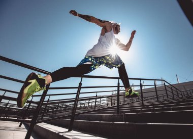 Modern spor giyim yakışıklı genç kaslı adam parlak güneşli bir gün merdivenleri açık yukarı çalıştırın. Jogging yapan bir adamın geniş açı fotoğrafı. Spor yaşam tarzı