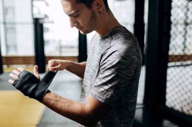 Gri tişört giymiş adam boks spor salonunda elinde bir el bandaj sarar
