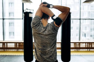 Koyu saçlı adam panoramik pencerelerin arka planda iki delme torbaları arasında spor salonunda kollarını uzanır