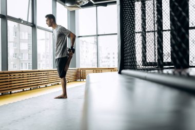 Gri tişört giymiş adam panoramik pencereleri ile boks spor salonunda kollarını uzanır