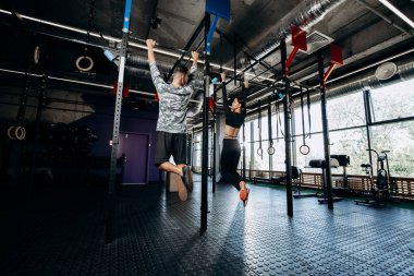İnce kız ve atletik erkek spor kıyafetlerini giymiş salonunda çubuğunda yukarı çekerek