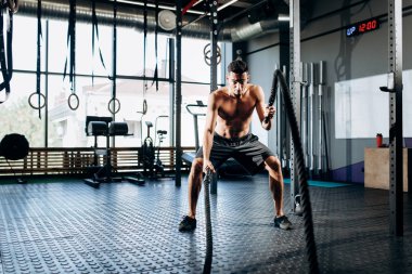 Çıplak bir gövde ile genç atletik adam jimnastik salonunda spor işleri ile spor egzersizleri yapıyor siyah şort giymiş