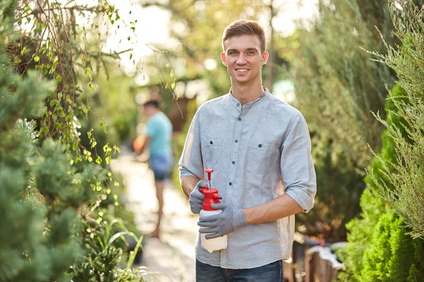 De tuinman van de kerel spuit water op installaties in de mooie kwekerij-tuin op een zonnige dag. Werk in de tuinman — Stockfoto