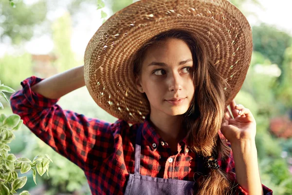 Чарівна дівчина садівник в солом'яному капелюсі стоїть в чудовому саду в сонячний день . — стокове фото