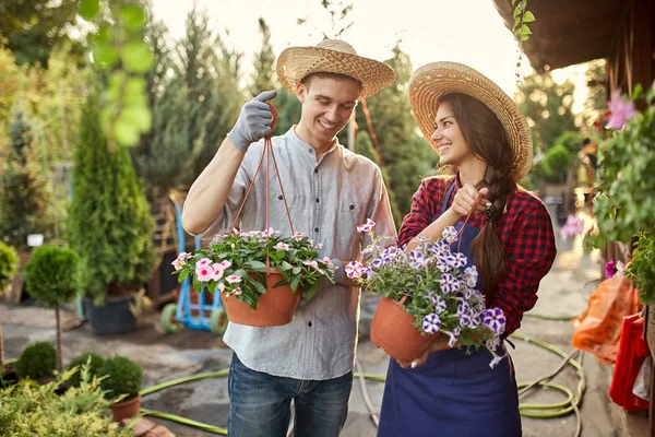 Feliz chico y chica jardineros en un sombreros de paja sostienen ollas con petunia en el camino del jardín en un día soleado . — Foto de Stock