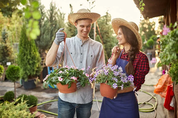 Feliz chico y chica jardineros en un sombreros de paja sostienen ollas con petunia en el camino del jardín en un día soleado . — Foto de Stock