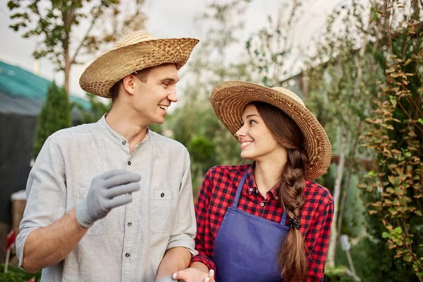 Cara sorridente e jardineiros de menina em um chapéu de palha olham um para o outro no jardim em um dia ensolarado . — Fotografia de Stock