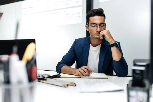 Mørkhåret ung arkitekt med briller og blå jakke jobber med dokumenter på kontoret – stockfoto