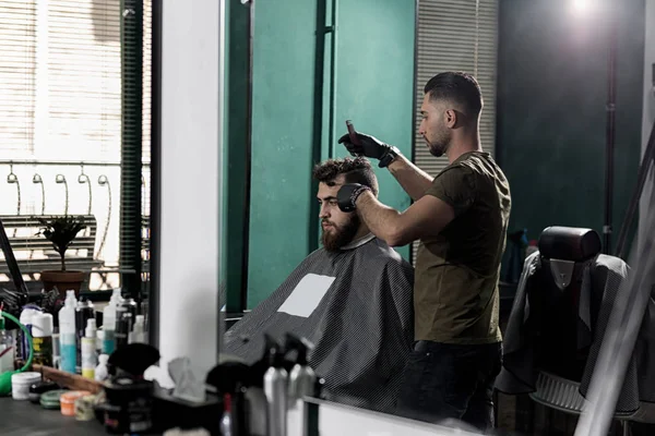 Жестокий человек в парикмахерской. Парикмахер расчесывает волосы перед зеркалом . — стоковое фото