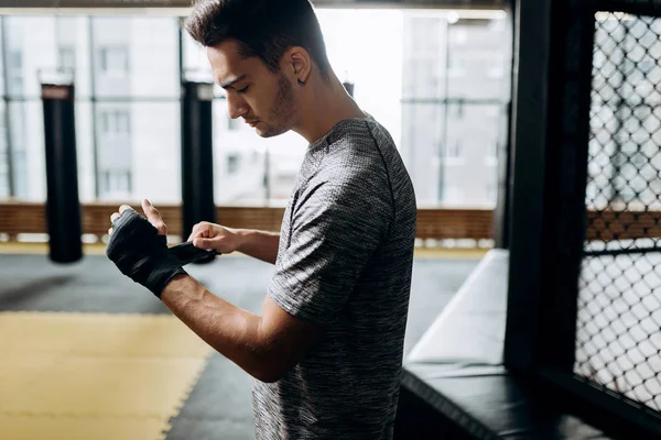 Gri tişört giymiş adam boks spor salonunda elinde bir el bandaj sarar — Stok fotoğraf