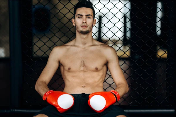 Sportsman com um tronco nu e as luvas de boxe vermelho em suas mãos senta-se na borda do anel de boxe — Fotografia de Stock