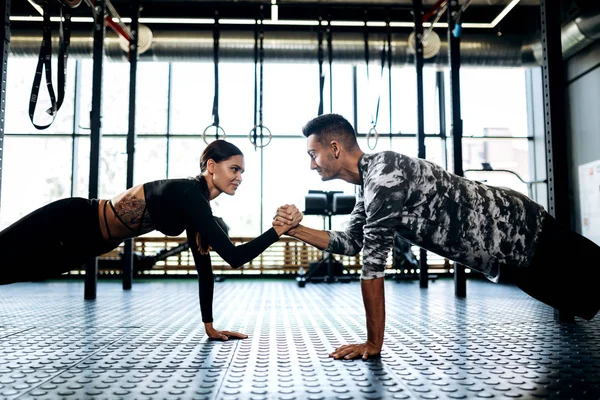 Młody sportowiec mężczyzna i kobieta robią deski i trzymając rękę w ręku w siłowni — Zdjęcie stockowe