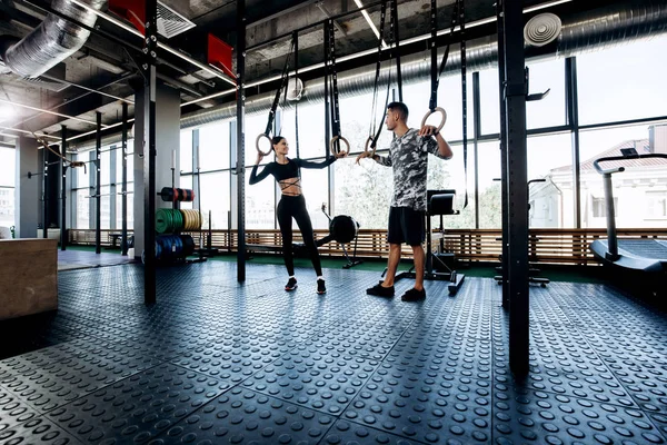 Mooie slanke donkerharige meisje gekleed zwarte sportkleding en atletische man praten in de sportschool — Stockfoto