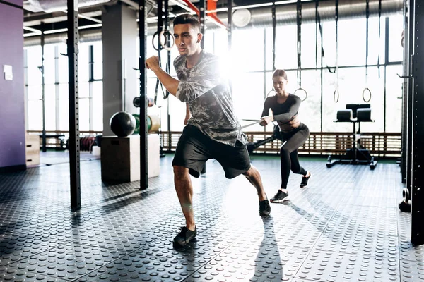 Homem atlético jovem e menina magro estão fazendo exercícios esportivos com equipamentos especiais, como banda de poder no ginásio — Fotografia de Stock