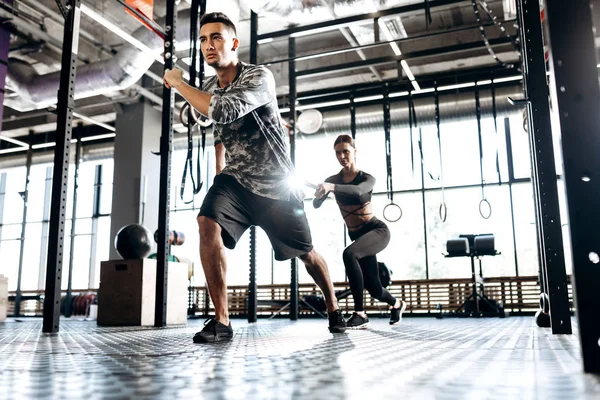 Junger athletischer Mann und schlankes Mädchen machen in der Turnhalle Sportübungen mit speziellen Geräten wie Kraftband — Stockfoto