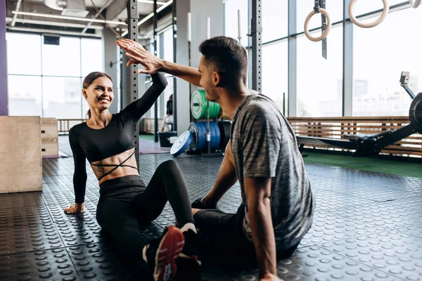 İnce kız ve spor giysileri giymiş genç adam katta oturuyor ve spor salonunda beş vermek