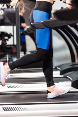 Spor giyinmiş atletik kız modern spor salonunda pencerelerin önünde koşu bandı üzerinde çalışıyor