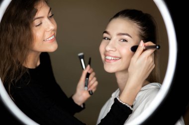 Makyaj sanatçısı çekici kız aynada yansıması için güzel bir genç kız makyaj yapıyor