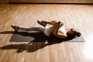 Muhteşem ince koyu saçlı kız beyaz spor üst ve tayt giyinmiş spor salonunda fitness için mat germe yapıyor