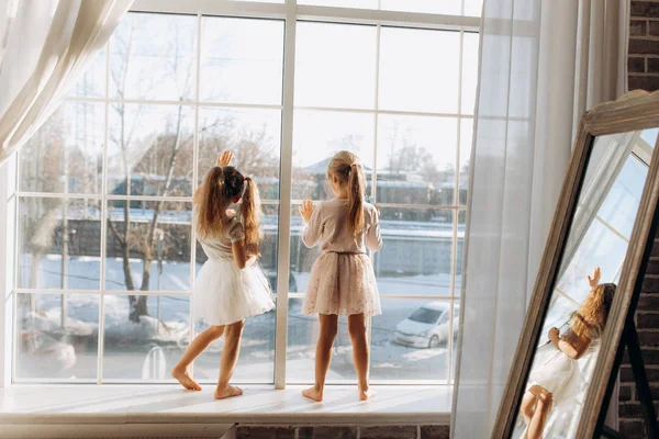 Dos hermanitas vestidas con los hermosos vestidos se paran en el alféizar de la ventana junto al espejo — Foto de Stock