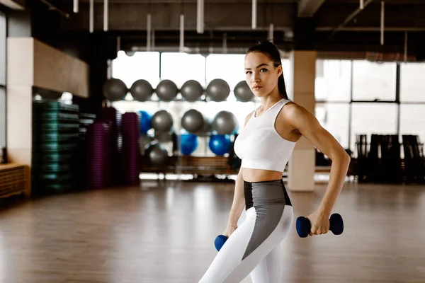 Mooi atletisch meisje gekleed in witte sporttop en panty's bouwt spieren op met dumbbells — Stockfoto