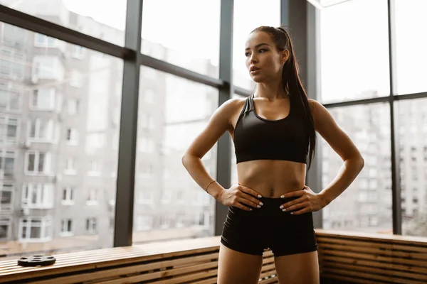 Bella ragazza atletica con i capelli castani vestita con top sportivo nero e pantaloncini stand in palestra — Foto Stock