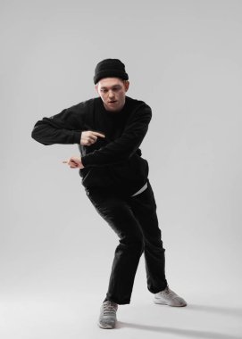 Siyah kot pantolon, kapüşonlu, şapkalı ve gri spor ayakkabı giyen adam beyaz arka plan üzerinde stüdyoda dans ediyor