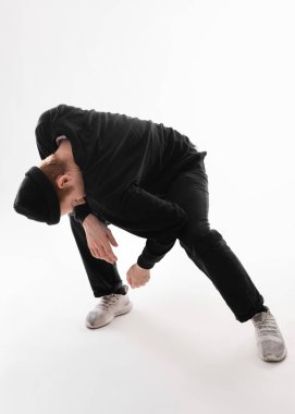 Siyah kot pantolon, sweatshirt, şapka ve gri spor ayakkabı giymiş Adam beyaz arka plan üzerinde stüdyoda öne eğilerek duruyor