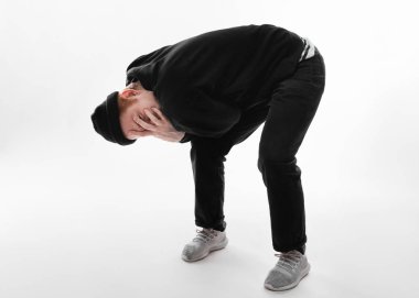 Siyah kot pantolon, kazak, şapka ve gri spor ayakkabı giymiş adam beyaz arka plan üzerinde stüdyoda elleriyle yüzünü kapatarak öne eğilerek duruyor