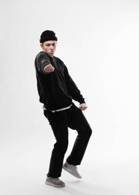 Young freestyle dancer dressed in black jeans, sweatshirt, hat and gray sneakers is dancing in the studio on the white background clipart