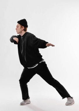 Genç dansçı siyah kot, tişört, şapka ve gri spor ayakkabı giymiş freestyle beyaz arka plan üzerinde stüdyoda dans ediyor