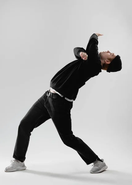 Guy dançarina vestida com jeans pretos, camisola, chapéu e tênis cinza está dançando no estúdio no fundo branco — Fotografia de Stock