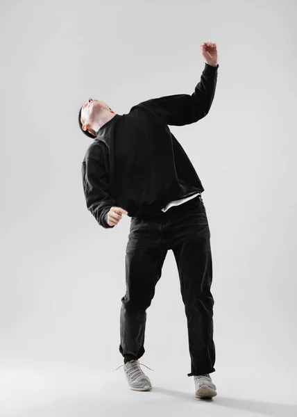 Ballerina vestita in jeans neri, felpa, cappello e sneakers grigie sta ballando in studio sullo sfondo bianco — Foto Stock