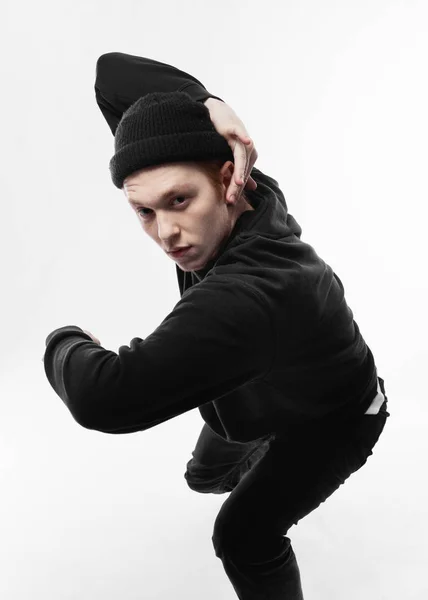 Jeune danseuse freestyle vêtue de jeans noirs, sweat-shirt, chapeau et baskets grises danse en studio sur fond blanc — Photo