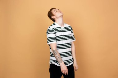 Çizgili bir gömlek ve siyah kot elindeki dövme olan Kızıl saçlı şık adam stüdyo bej renkli arka plan üzerinde duruyor