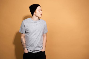 Şık adam gri gömlek giymiş, siyah kot pantolon ve siyah şapka stüdyoda bej arka planda poz